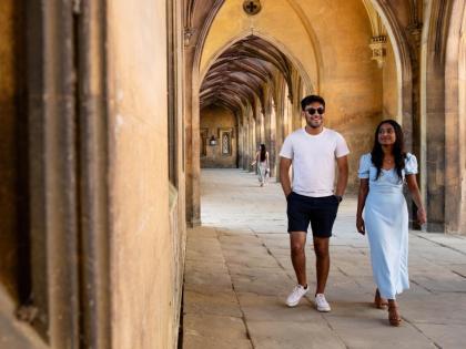 Two people walking down a corridor that is made up of arches. 
